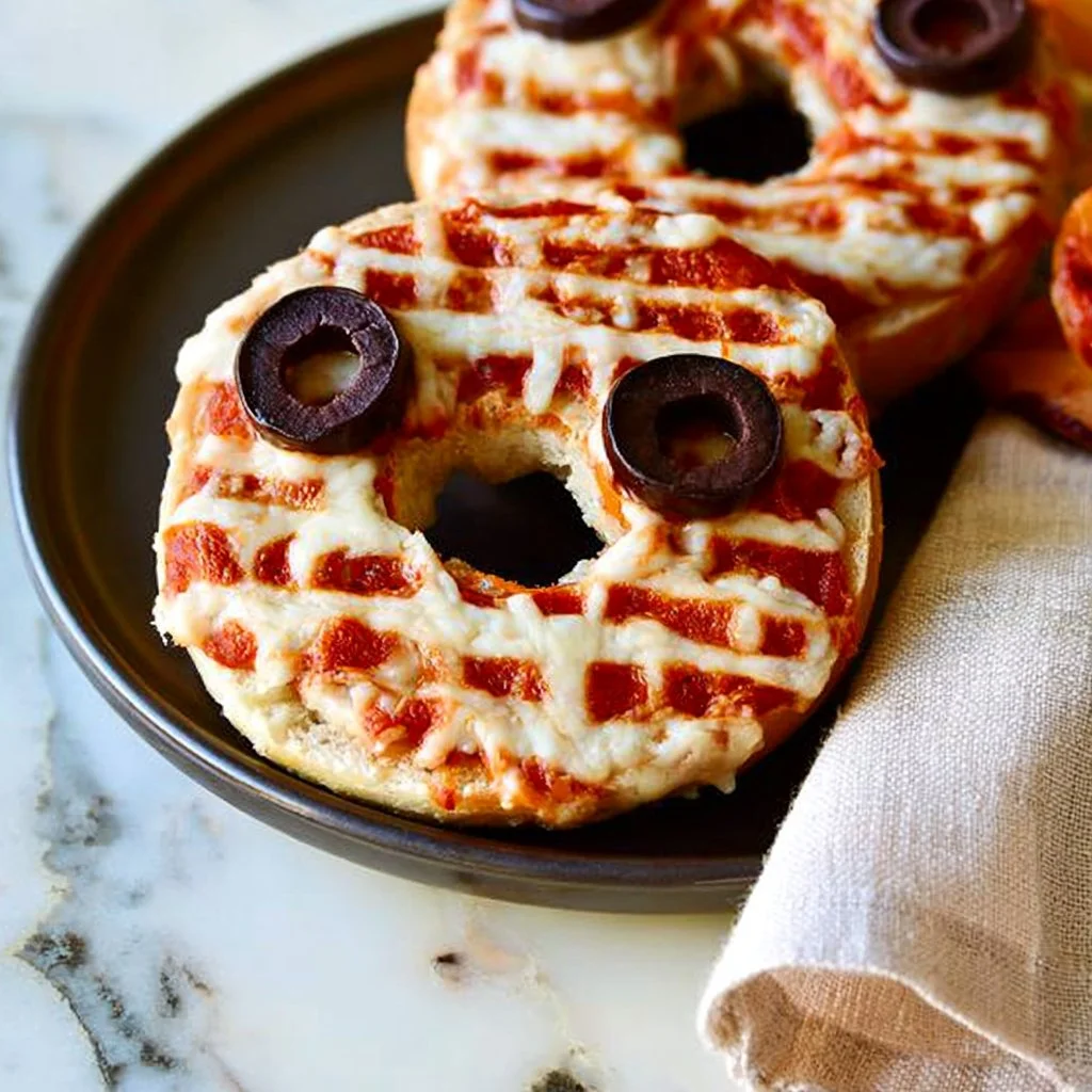 Plate of Pizza Bagel Monsters with olive eyes, creative snack idea for kids.
