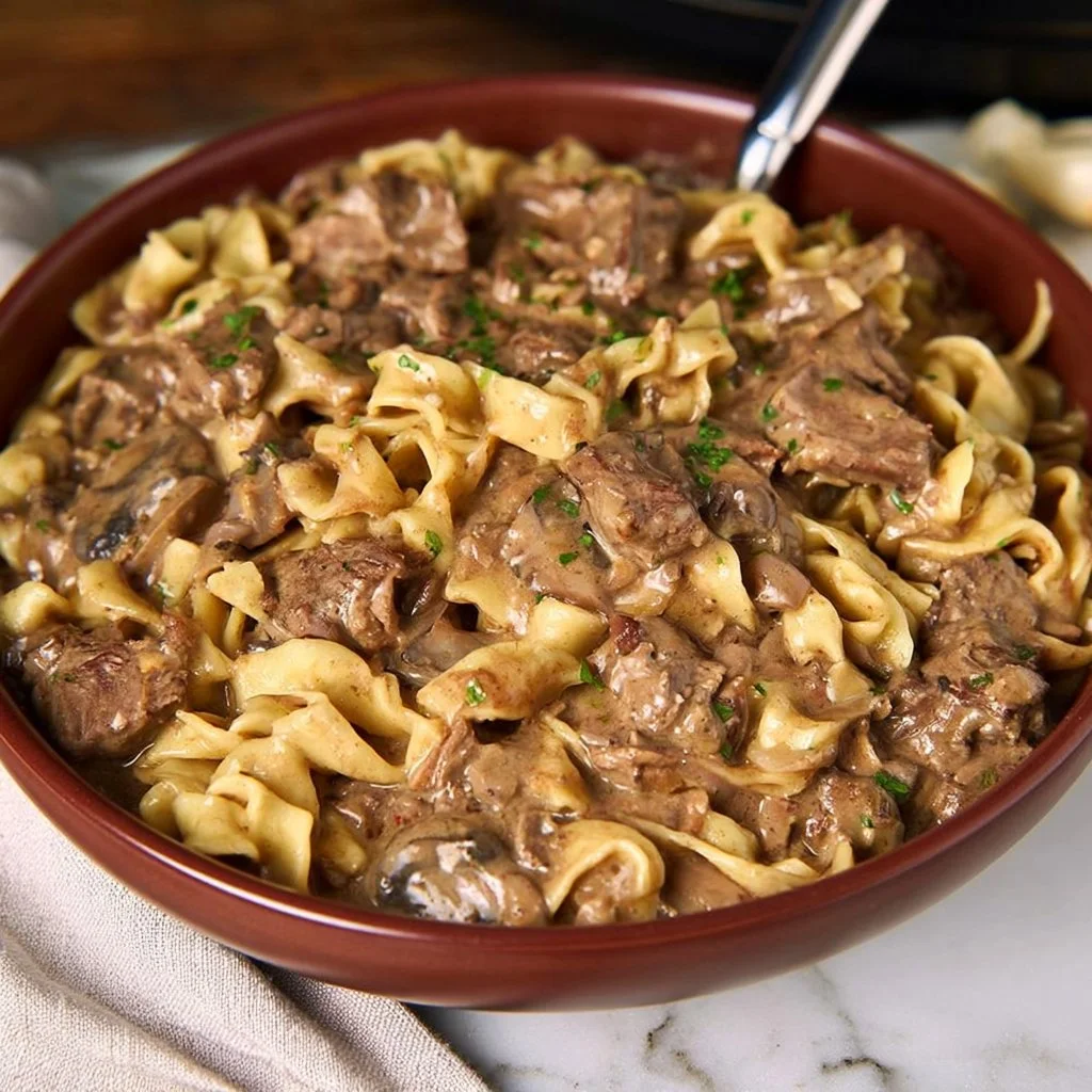 Delicious slow cooker beef stroganoff served on a plate with noodles and garnished.